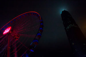 Red light illuminated ferris wheel next to skyscraper by the night, harbor, Hongkong Red light illuminated ferris wheel next to skyscraper by the night, harbor, Hongkong